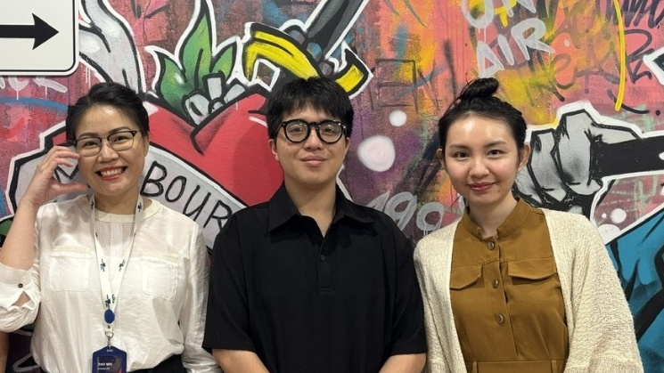 Three people posing in front of the graffiti wall at the Ho Chi Minh City Hub 