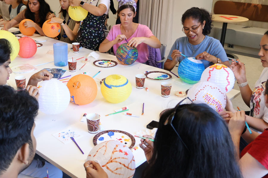 Photograph shows children and adults crafting colorful paper lanterns at a communal table.