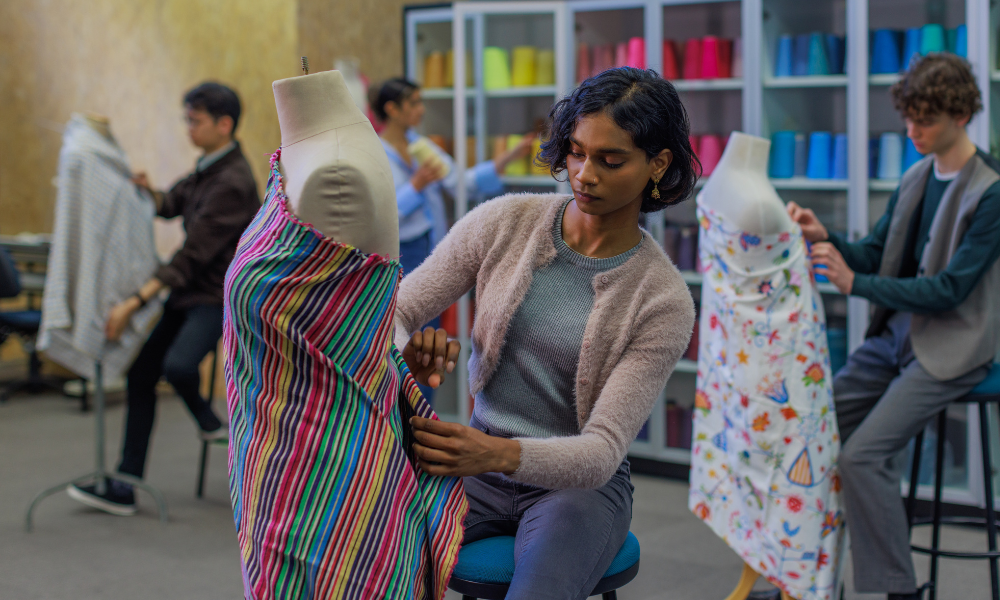 Photograph of a fashion design studio showing a designer fitting bright multicolored striped fabric onto a mannequin.