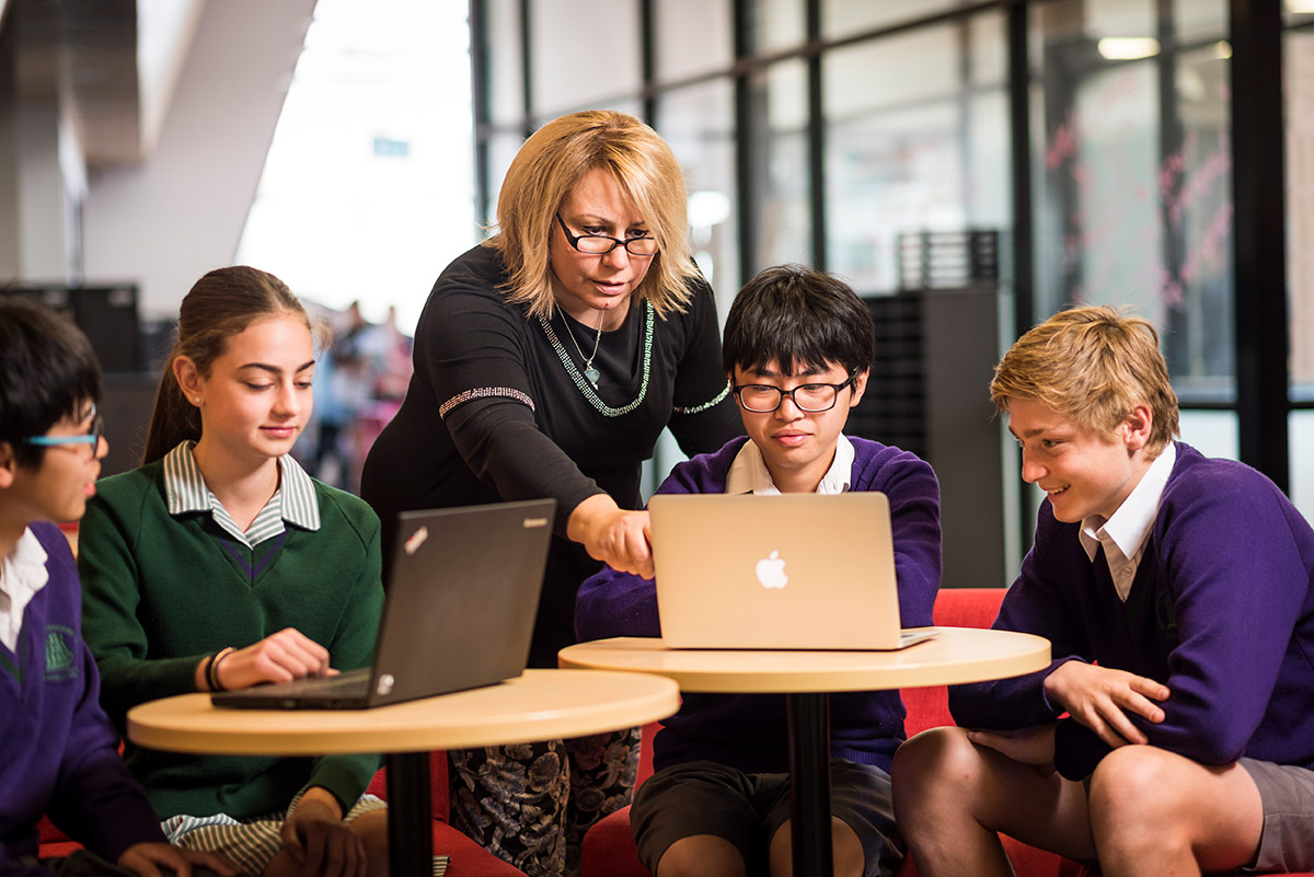 School kids working with teacher on laptops