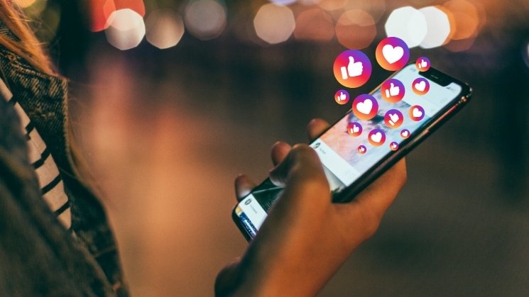 Student holding mobile phone, instagram hearts and thumbs up graphic overlay