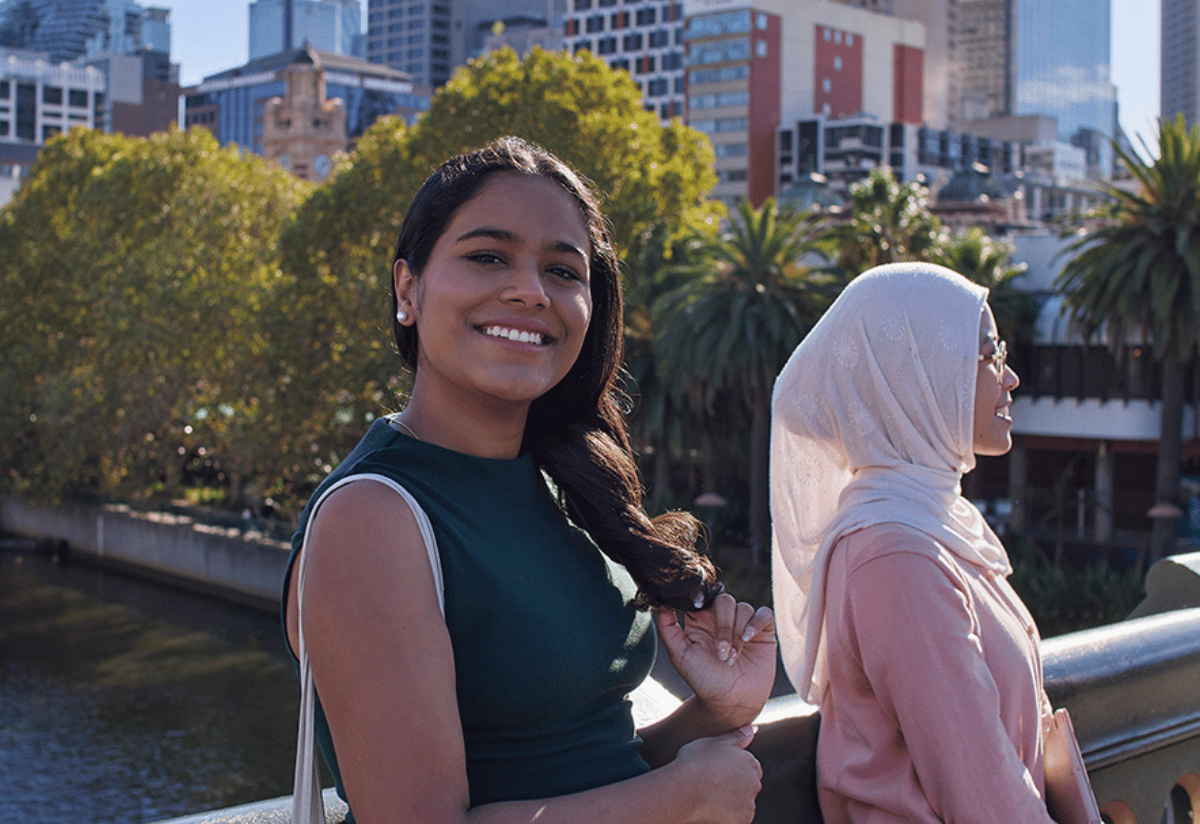 Photograph of three people standing outdoors near a railing with urban buildings and trees in the background