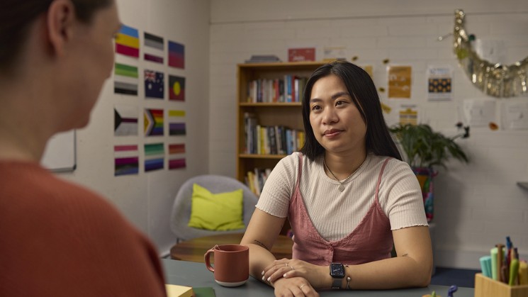 Student speaking with counselor in office, flags on the world and bookshelf in background 