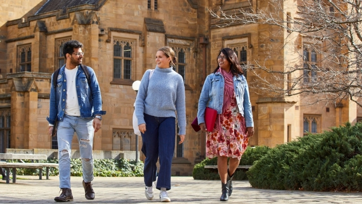 Group of international students sitting on the lawn at Melbourne University, iconic clock tower in the background