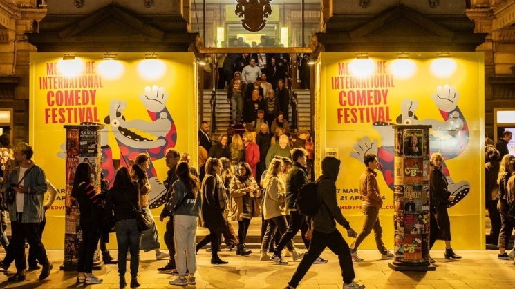 Town Hall with Melbourne International Comedy Festival branding, night time, lots of people walking by