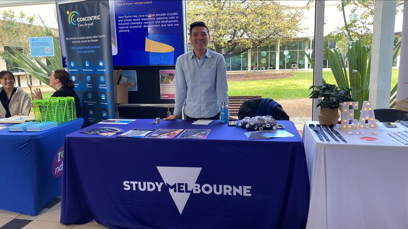 Photograph of an informational booth at an outdoor event featuring a blue tablecloth with brochures, green cups, and promotional items.