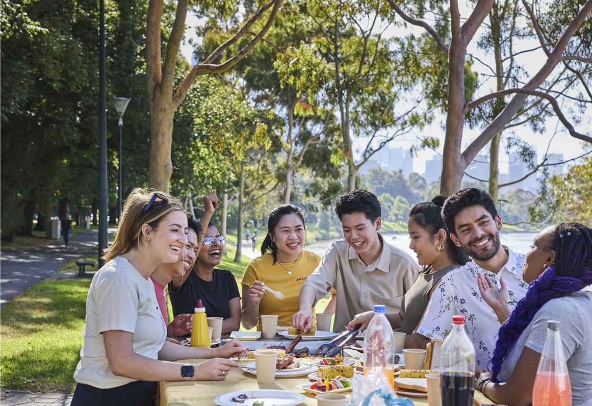 Students enjoying a bbq picnic on next to the Yarra river, city skyline in background