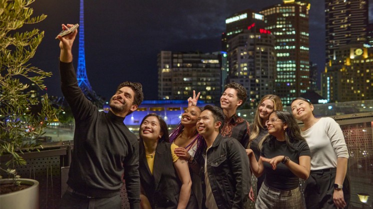 Students out a night in Melbourne city taking a group selfie, Arts Centre spire and high rise buildings in background