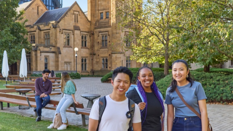 Students enjoying campus life at the University of Melbourne, heritage buildings in background with trees and lawn