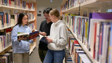Three students in a library looking at books