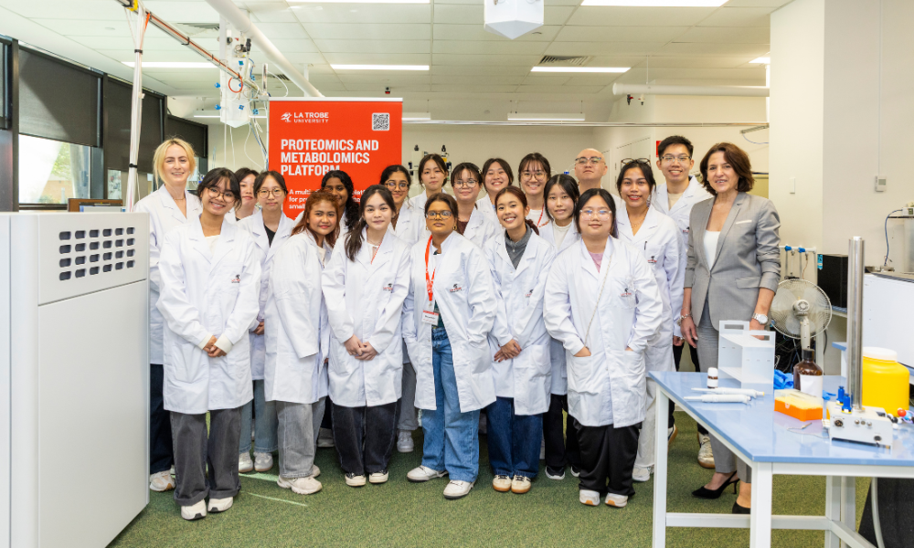 Photograph of a diverse group of scientists and researchers wearing white lab coats posing in a laboratory setting. 