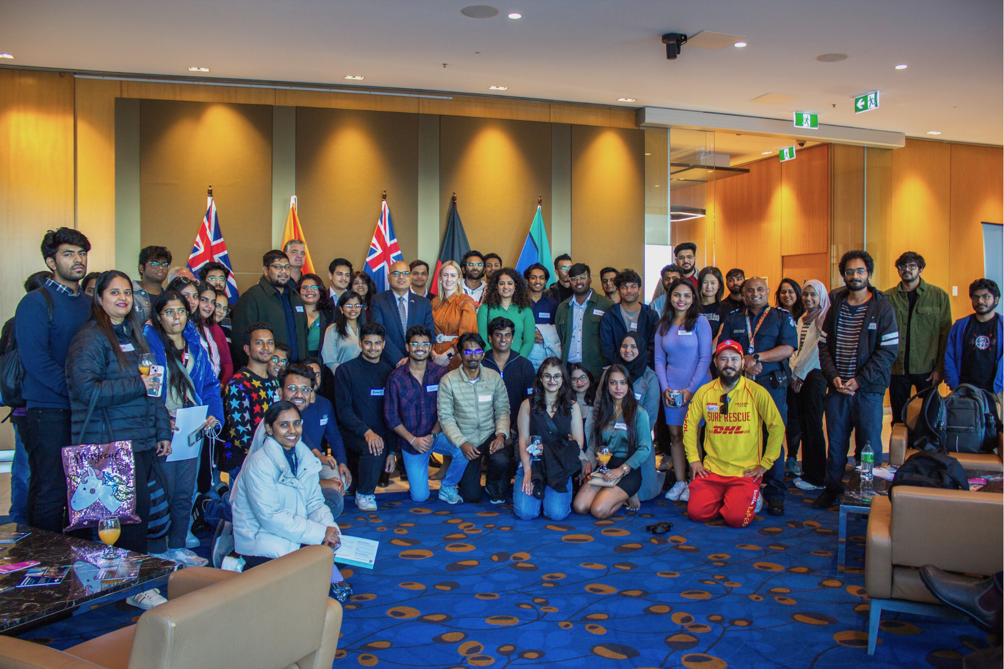 A photograph of a large diverse group of people posing indoors with flags. 