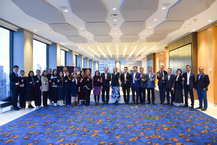Photograph of a large group of professionally dressed individuals standing in a modern office space with floor-to-ceiling windows and cityscape view. 