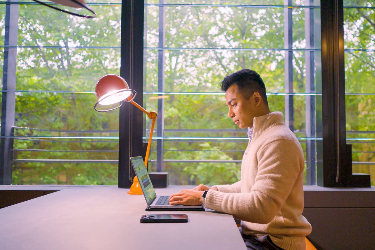 Student working on a laptop, trees in background out the window