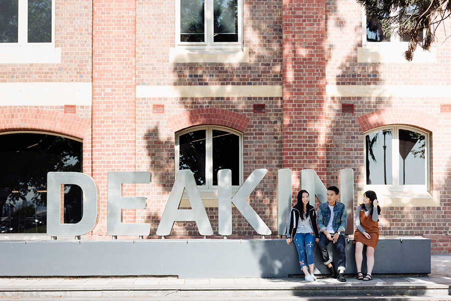 Warehouse style building with large Deakin branding in foreground, students sitting to the side