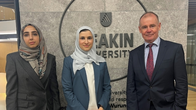 Three delegates standing in front of Deakin University signage