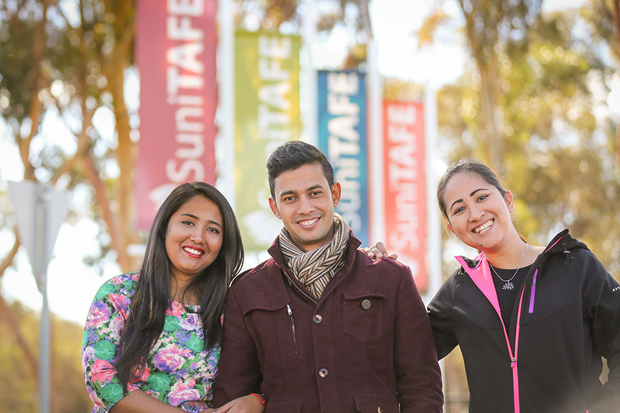 Three students in front of TAFE signs