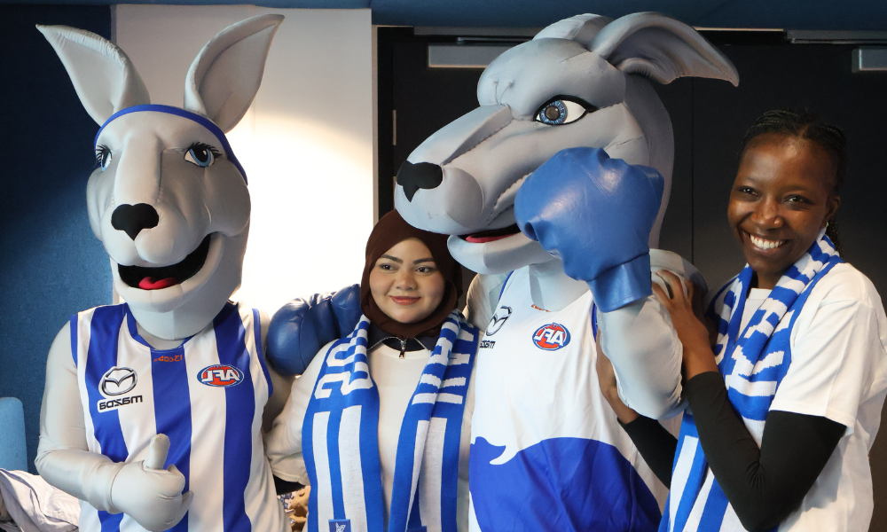 Photograph of two people posing with two kangaroo mascots dressed in blue and white Australian Football League (AFL) team uniforms.