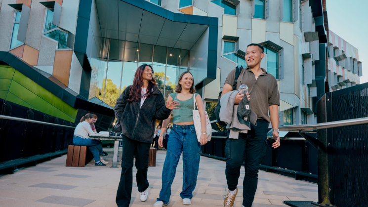 3 students walking in front of a honeycomb building design of Latrobe university campus. Latrobe University logo overlayed.