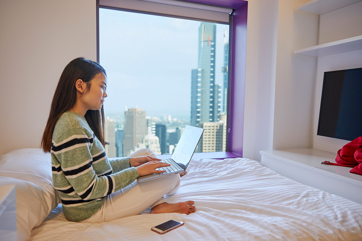 Student sitting on bed with Melbourne skyline out the window