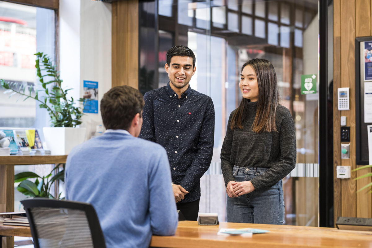 Two students speaking to person sitting at desk