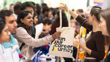 Stand at careers fair, showbag with Plan your career journey is being passed to a student