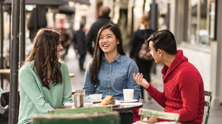 Three students enjoying coffee and cake at a laneway cafe