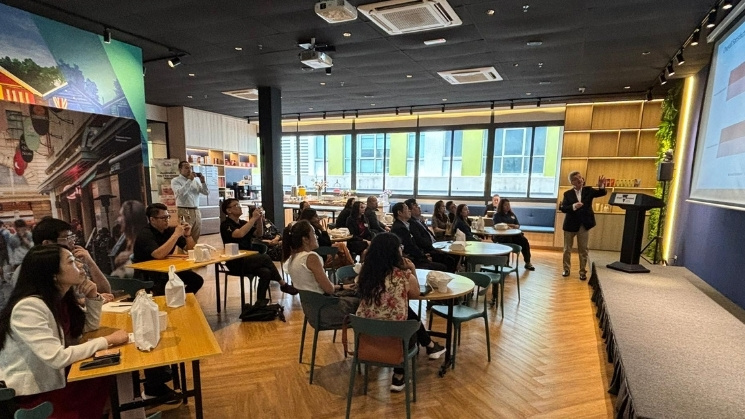 Presentation of the Student Satisfaction Report at the KL hub, table seating with projector screen and Melbourne themed artwork in the background