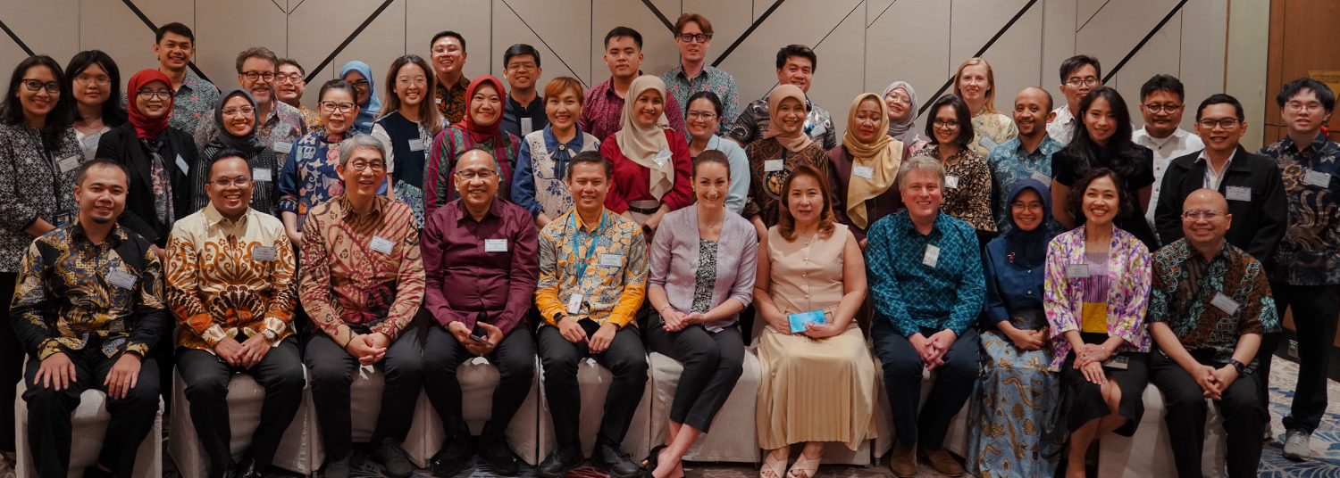 Group photograph of diverse adults arranged in two rows, dressed in colorful and patterned formal attire, posing indoors against a geometric wall backdrop. 