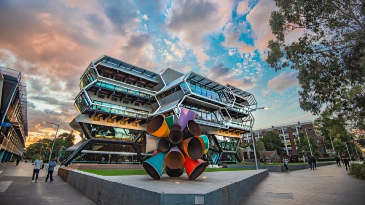 Monash University campus, moody sky, trees and students as well as abstract outdoor artwork