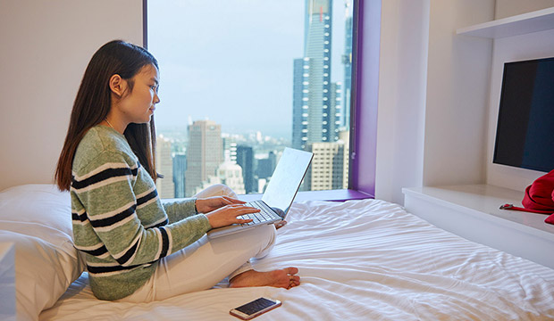 Student sitting on bed with Melbourne skyline out the window