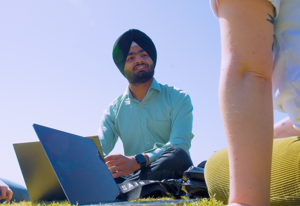 Photograph of two people sitting outdoors with laptops engaged in discussion.