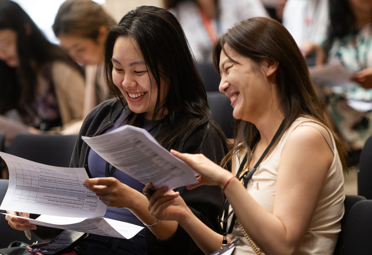 Photograph of a group of people seated indoors, focusing on two individuals reviewing printed documents with charts and text.
