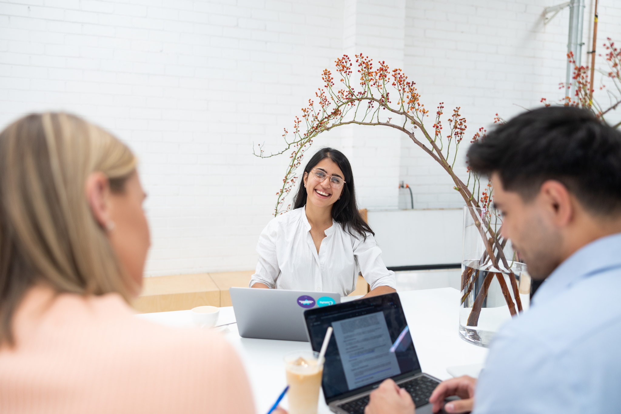 Photograph of three people engaged in a meeting or discussion around a table with laptops. 