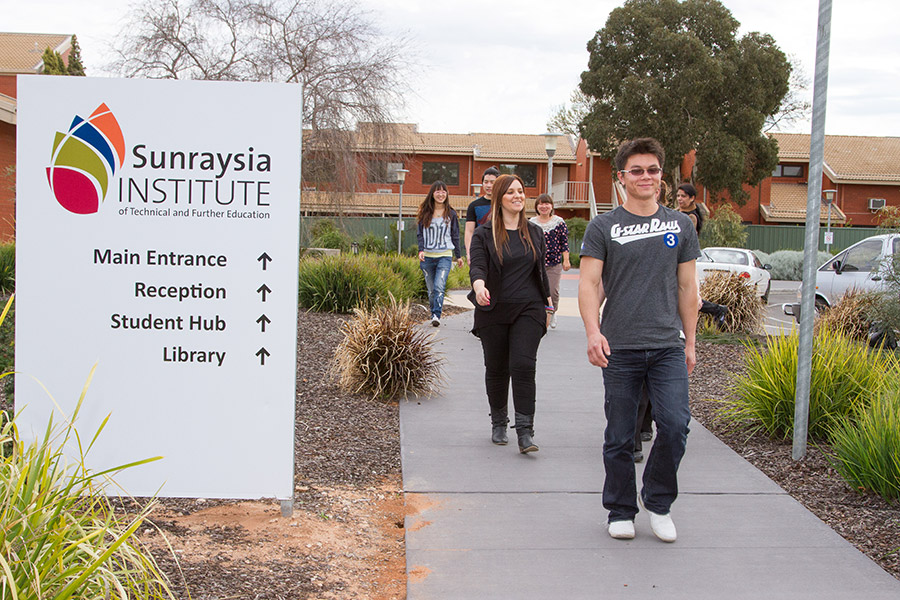 Students walking out the front of SuniTAFE campus, branding in foreground, signage pointing to Main entrance, Reception, Student Hub and Library