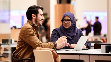 Two people talking, laptop in front