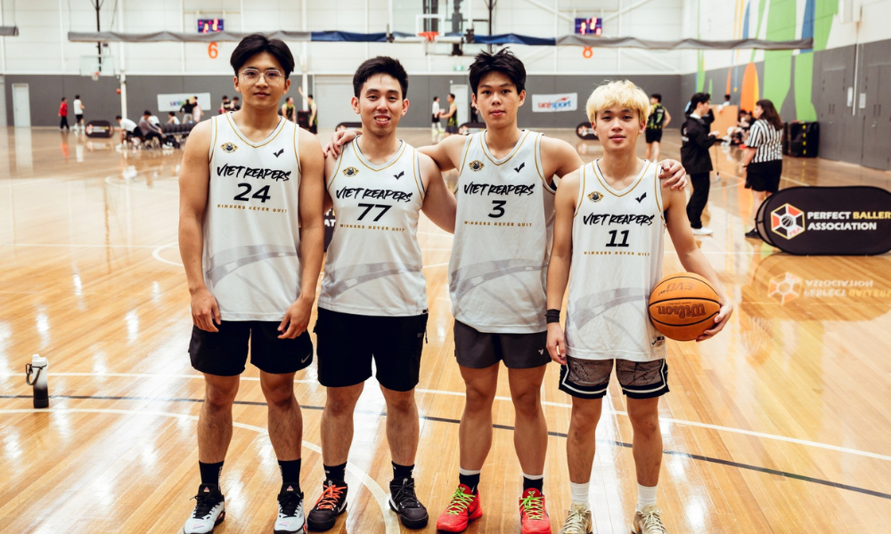Photograph of four male basketball players posing on an indoor court.