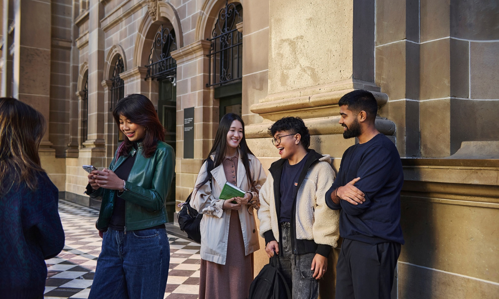 Group of international students sitting on the lawn at Melbourne University, iconic clock tower in the background