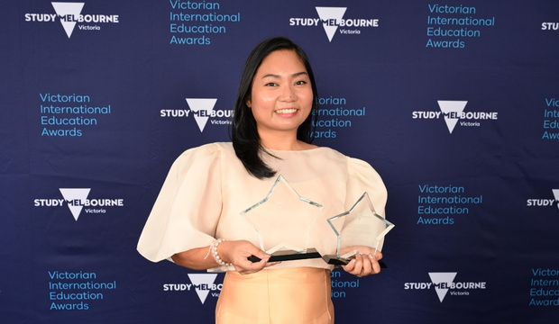 Portrait of Lara with two star shaped trophies, Study Melbourne Victoria and Victorian International Education Awards branding in background