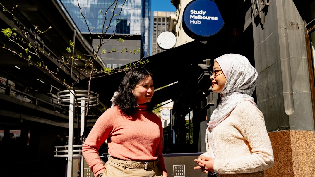 Two international students talking in front of heritage building with Study Melbourne Hub branding