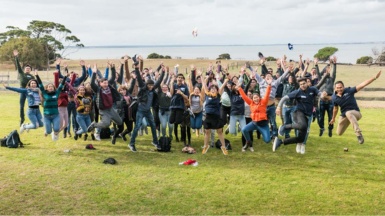 Large group of students jumping and posing for the camera, bay in the background